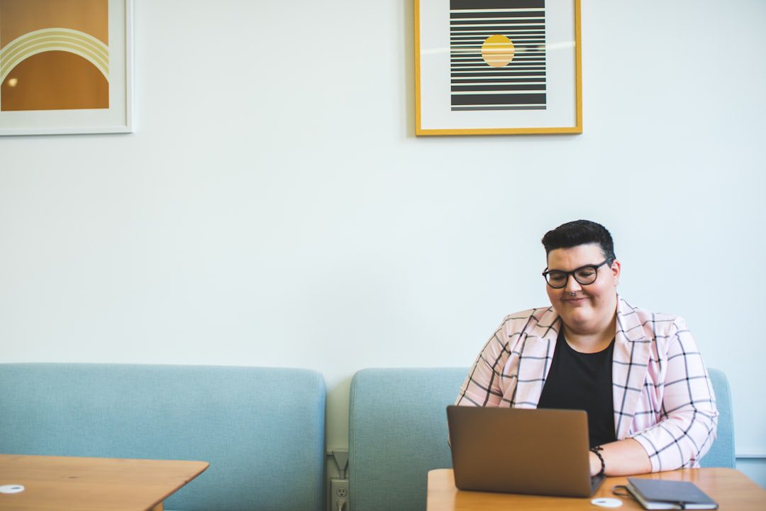 A person sitting in their current home takes a virtual tour of a bright, modern living room on their laptop, illustrating the process of buying a home sight unseen.