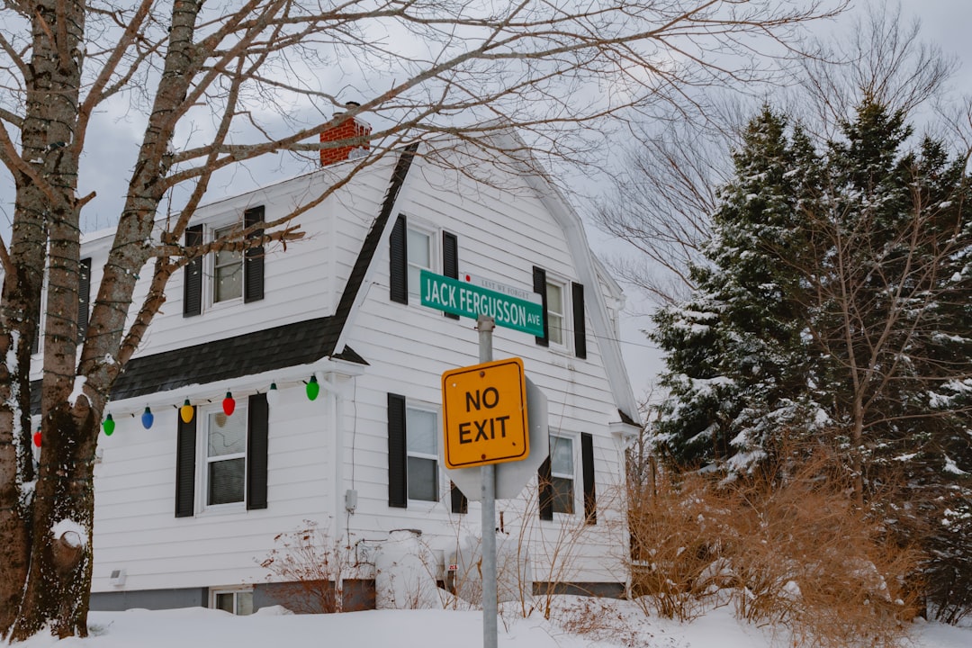 A close-up of a 'For Sale' sign in front of a residential home, with a bright red 'Price Reduced' sticker clearly visible, representing a financial loss for the seller.