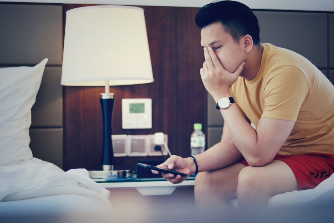 A landlord looking stressed and tired while on the phone and reviewing paperwork late at night in a dimly lit room, representing the overwhelm of property management.