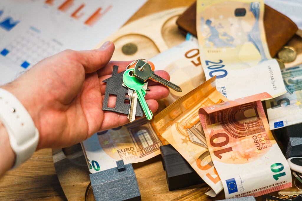 Person sits at a modern, clean desk, thoughtfully looking at house keys next to a calculator, contemplating a financial de...