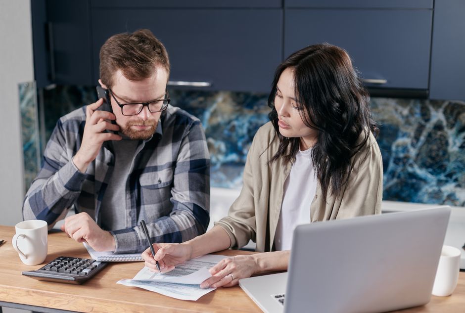 A couple sits at a bright kitchen island, looking at a laptop together as they search for the best realtor to help with their home purchase.