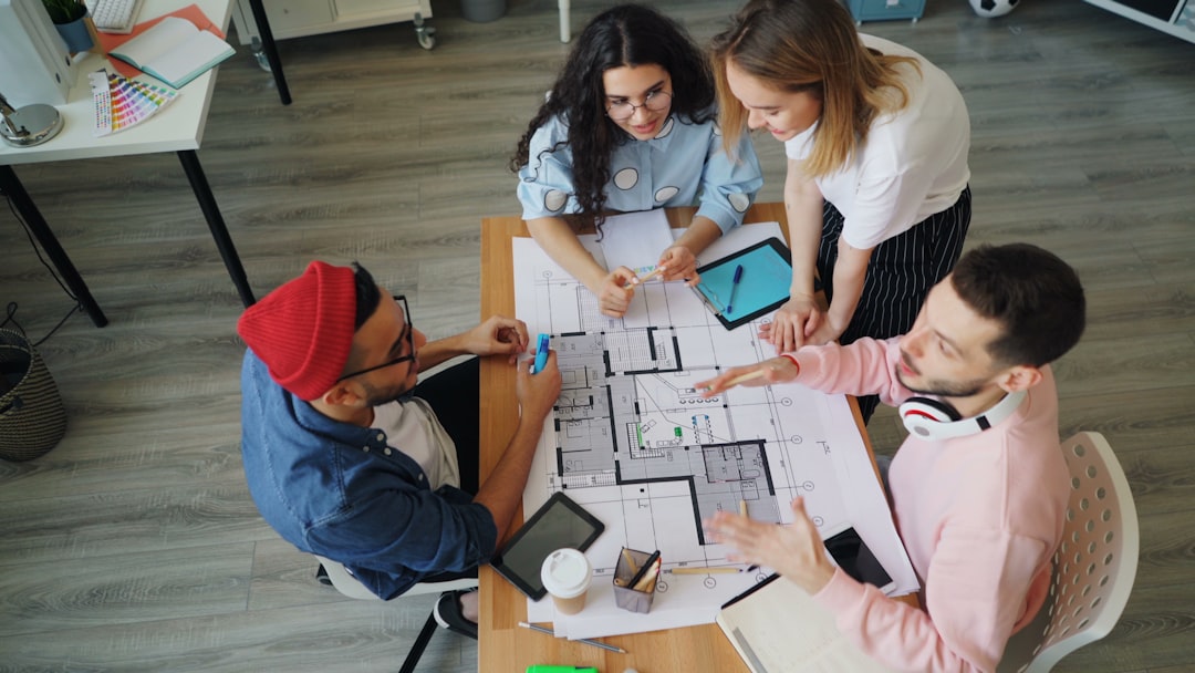 A team of diverse professionals in a bright, modern office gathered around a table, strategically planning with an architectural model of a house, representing expertise in real estate transactions.
