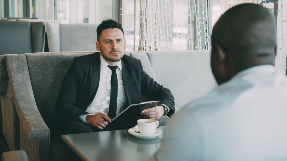 Homeowner and a real estate agent have a serious discussion across a modern table, representing the 'stress test' intervie...